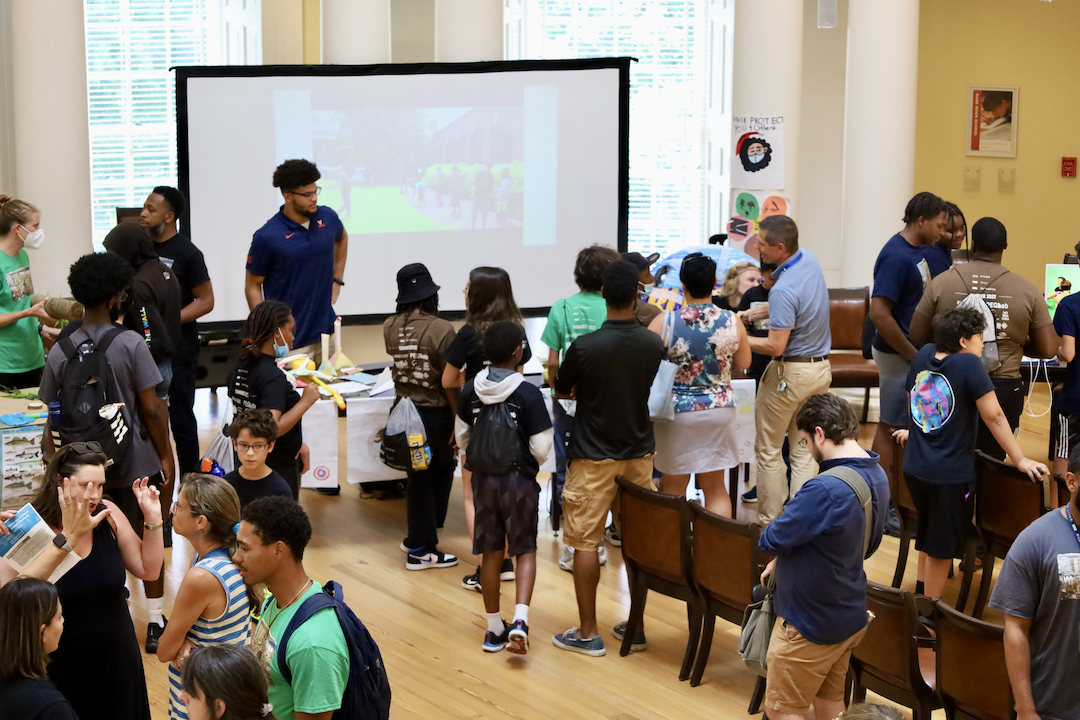 Image shows a large room with middle-school aged children at an expo showing what they learned during a summer program.